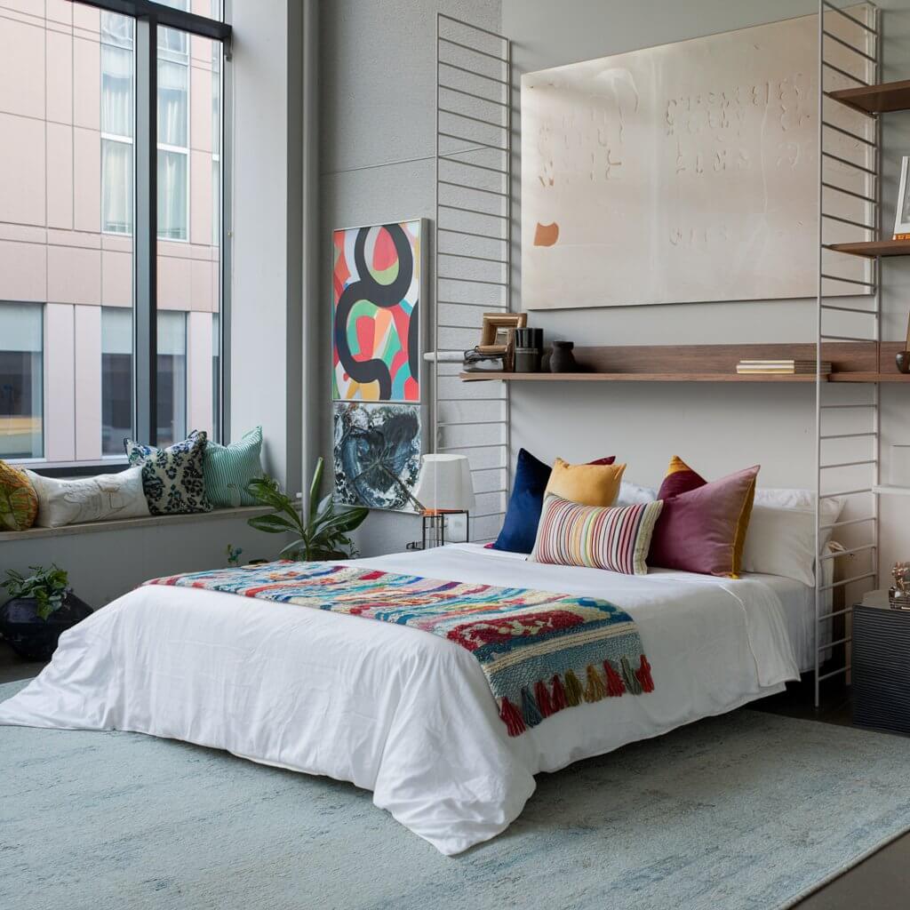 12 Stunning Urban Bedroom Ideas You Need to Try 9 Stylish urban bedroom featuring layered textiles for a cozy and modern aesthetic. The image showcases a mix of patterned throw blankets, plush pillows, and textured bedding that enhance the room's depth and warmth. Perfect for those seeking urban bedroom ideas that embrace comfort and contemporary design through creative textile combinations.